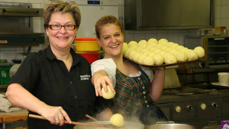 Bergwirt Schrammel & Mohnhotel, © Bergwirt Schrammel Two women in a kitchen, one holding a tray of dumplings, the other cooking dumplings in a pot.