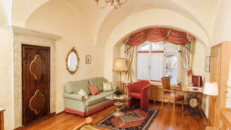 Kirchenwirt Weißenkirchen, © Rita Newman Cozy living room with antique flair, sofa, carpet, table and window with curtains.