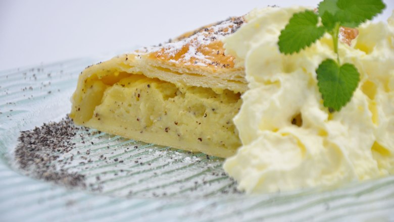 White poppy seed and pear strudel, © Café Pension Kristall A slice of white poppy seed and pear strudel with cream and mint leaf on a plate.