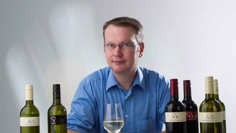 Christian Pleil, © Fotostudio Semrad Man in blue shirt with wine glass and wine bottles on a table.