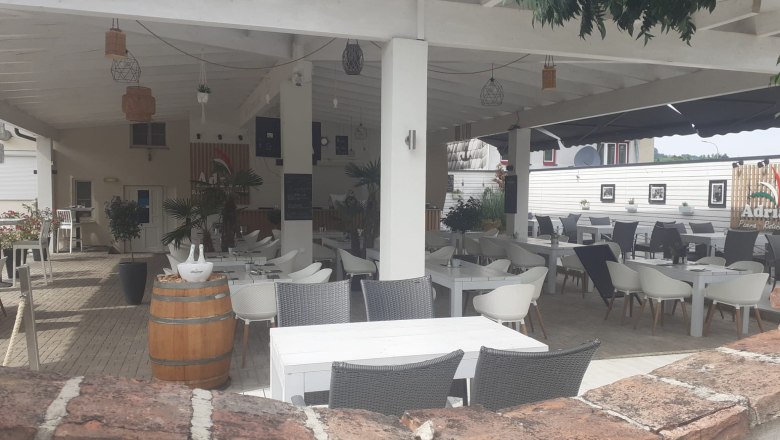 Cozy guest garden., © Wiener Alpen A covered guest garden with white tables and chairs, surrounded by plants and decorations.