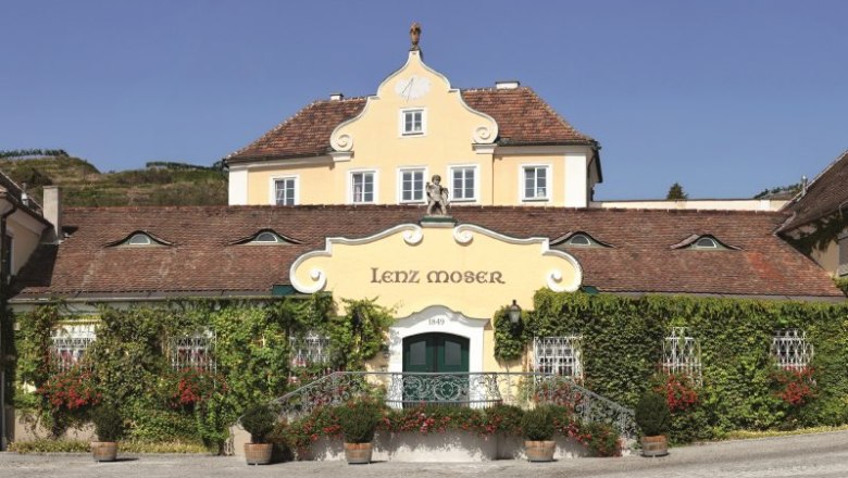 Lenz Moser, © Lenz Moser Historic building with the inscription 'Lenz Moser', surrounded by plants and flowers.