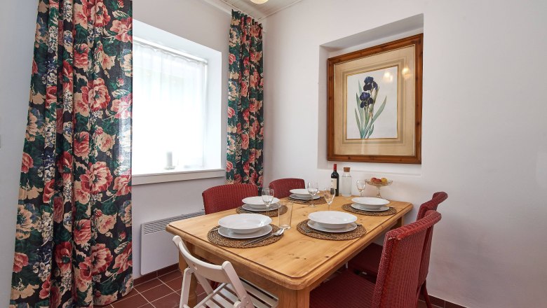 Top 4 - Dining table, © VP FeWo OG A dining table with four place settings, red chairs and a picture of flowers on the wall.