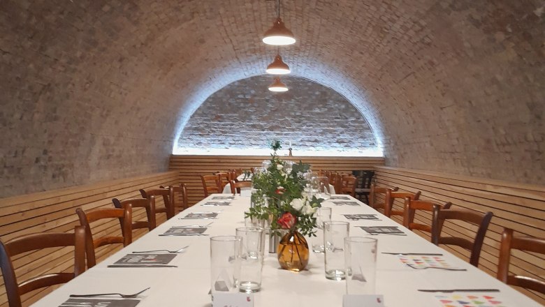 Distillery - Kollmann, Destithek, © Brennerei - Kollmann Long table in a vaulted cellar, laid with white tablecloths, glasses and flowers.