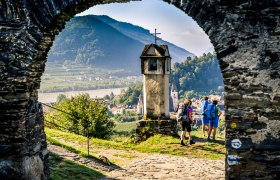 View from the Red Gate in Spitz, © Robert Herbst View through a stone gate onto a landscape with hills, a river and hikers.