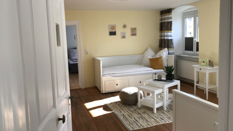 Common room, © Martina Braun Bright room with yellow walls, a white day bed, small table and plants.