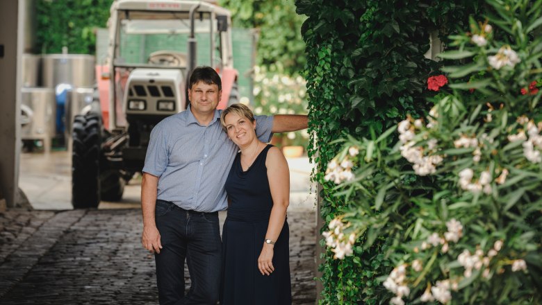Martin and Andrea Hirtl, © Michael Reidinger A couple stands under an ivy-covered canopy next to a tractor.