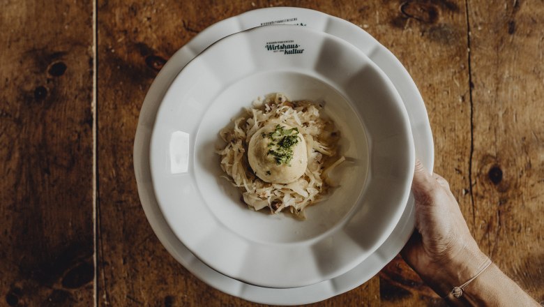 Grammelknödel, © Niederösterreich Werbung/Sophie Menegaldo A plate with a grammel dumpling on sauerkraut, held by one hand.