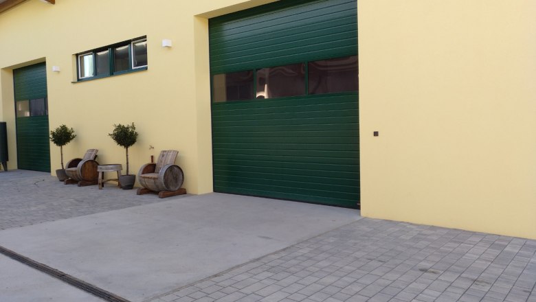 The cellar in Rohrendorf, © Weingut Mittelbach Yellow building with green gates and wooden furniture outside.