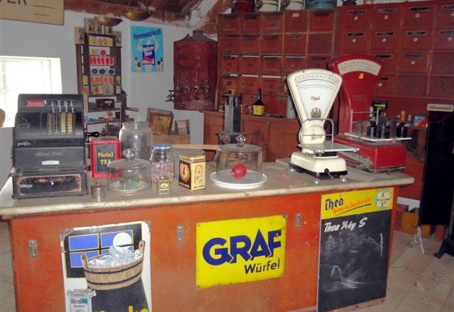 Museum for village culture in Grossengersdorf, © Museum für Dorfkultur in Grossengersdorf A historic village store with an old cash register, scales and various products on a counter.