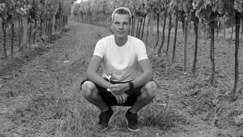 Roman Wagner, © Weingut Wagner Person squatting in a vineyard with a wine glass in his hand.