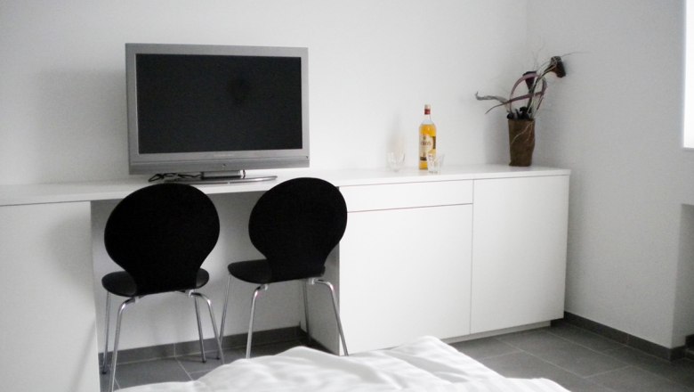 UHL workers' quarter, © Arbeiterquartier UHL Modern room with TV, two black chairs and white wardrobe.
