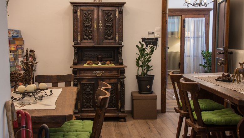 Common room, © Dirnbauer Cozy lounge with wooden furniture, green seat cushions and decorative cupboard.
