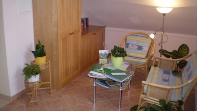 Reading corner, © Gästezimmer Rieder Cozy reading corner with rattan furniture, plants and a small table with books.