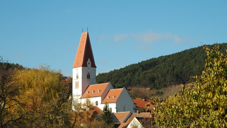 Church Nußdorf, © Blesl Church in Nußdorf with red roof and clock tower, surrounded by trees and hills.