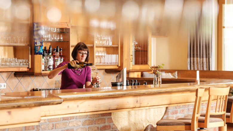 Wine.restaurant Neustifter, © Weinviertel Tourismus / Michael Reidinger A woman stands behind a bar in a rustic restaurant and pours wine.