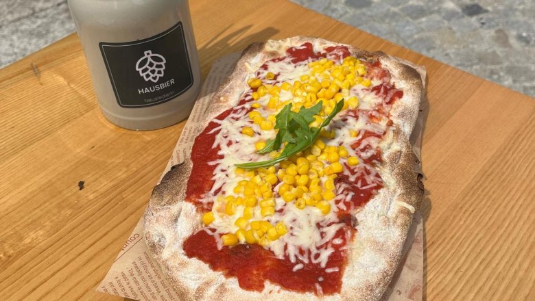 Sandwiches, "Die Neusiedlerin", Klein-Neusiedl, © Die Neusiedlerin Flatbread with corn and rocket served on a wooden board, next to a container with cutlery and napkins.