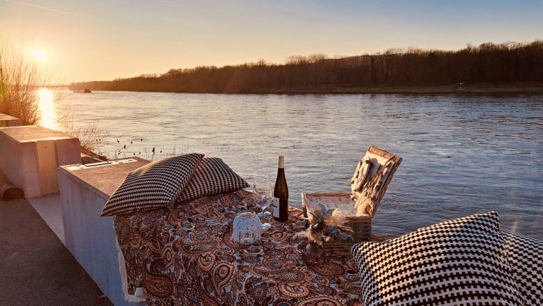 Romantic picnic spots, © Szilágyi Picnic on the riverbank at sunset with a blanket, cushion, wine and picnic basket.