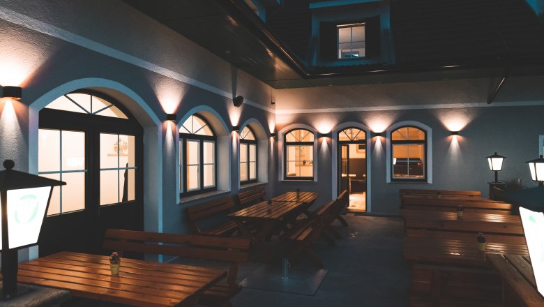 Hubertushof, © Matthias Auer Illuminated courtyard with wooden benches and tables, surrounded by a building with arched windows.