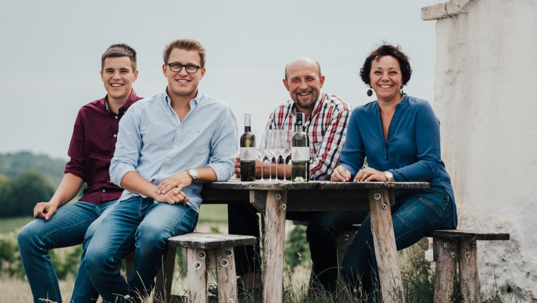 The Zimmermann family, © Winzerhof Zimmermann Four people sit at a wooden table outside with bottles of wine and glasses.