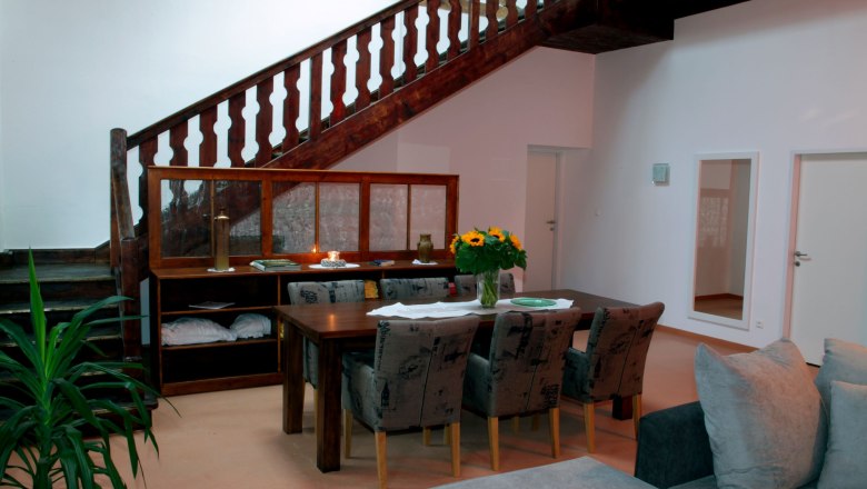 Dining area in loft 1, © Carlos de Mello Dining area in a loft with wooden table, chairs, stairs and plants.