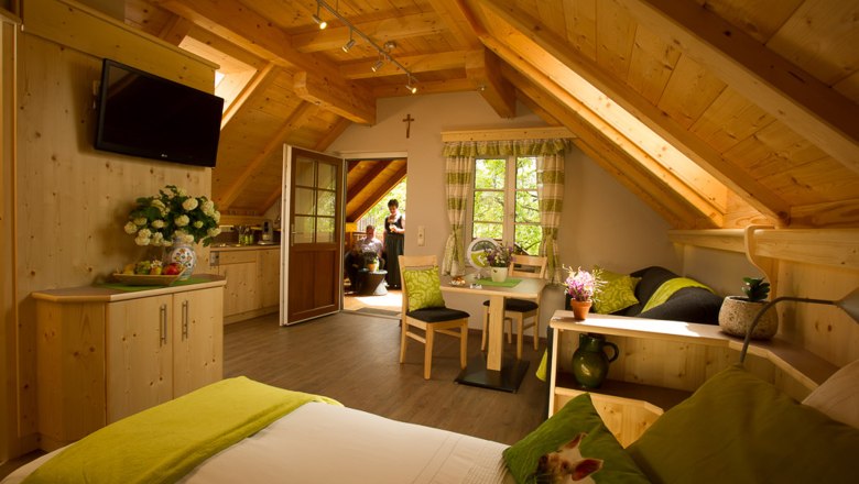 Vacation apartment at the farmer and landlord Langthaler, © Familie Langthaler Cozy vacation apartment with wooden furnishings, sloping ceilings and green accents. Two people can be seen on a balcony in the background.