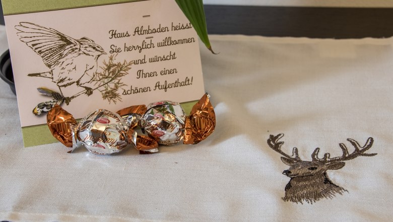 Double room Donkey, © Dirnbauer Welcome card with bird drawing and chocolates on a tablecloth with deer motif.