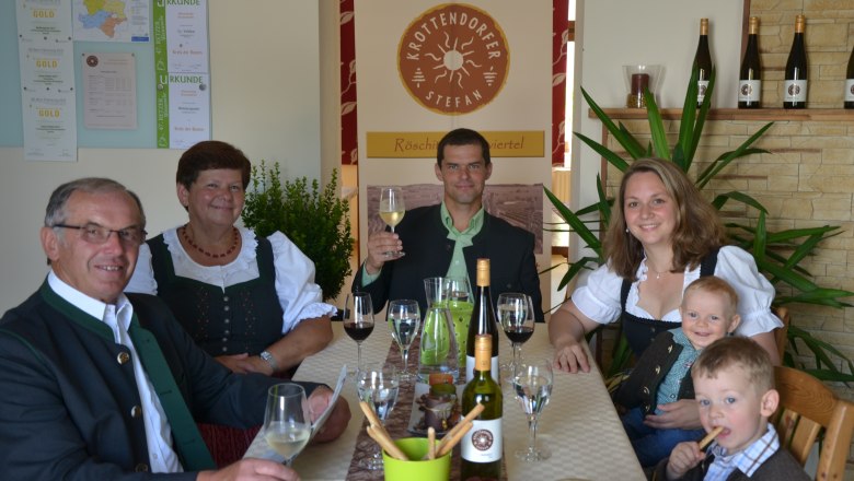 Krottendorfer family, © Familie Krottendorfer Family in traditional dress sitting at a table with wine and glasses.