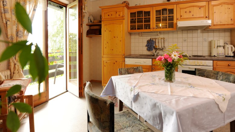 Apartment, © Steve Haider Cozy kitchen with wooden furniture, dining table and bouquet of flowers. Open balcony door with a view of the greenery.