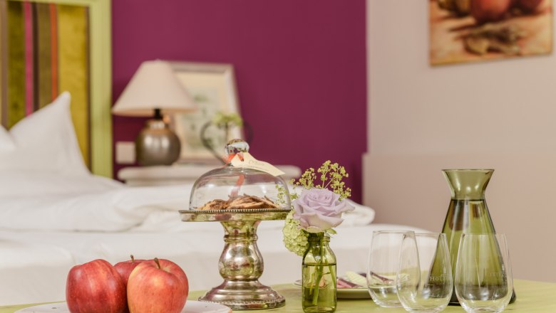 Room, © Rita Newman A stylishly furnished room with a table on which apples, cookies under a glass bell jar, a vase with a flower and glasses are placed.