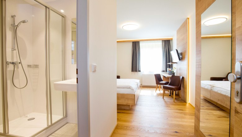 Room view, © Hotel Stich Modern hotel room with bathroom, bed, desk and chairs.