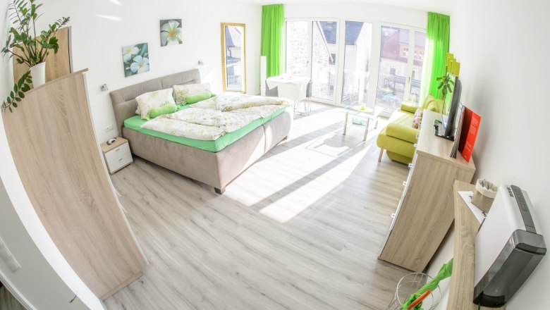 Guest rooms in the Haiminger guest house, © Gästehaus Schmelz Bright guest room with double bed, sofa, TV and large windows.