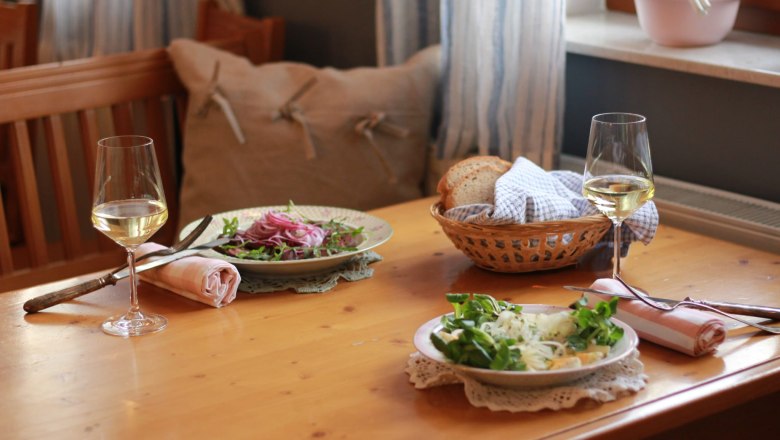 Buschenschank (typical tavern) Demmer, © Thomas Norek Two plates of salad and two glasses of white wine on a wooden table, with a bread basket next to them.