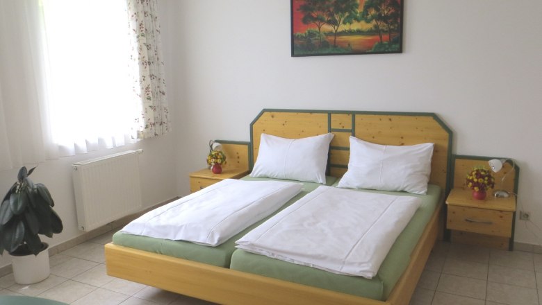 Guest room Nexing, © Urani A guest room with a double bed, bedside tables, a picture on the wall and a window with curtains.