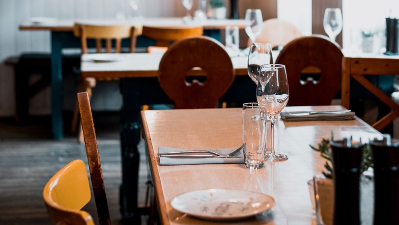 Urban pub flair, © Vinzenz Pauli/Philip Hinteregger A table set in a cozy restaurant with wooden furniture and wine glasses.