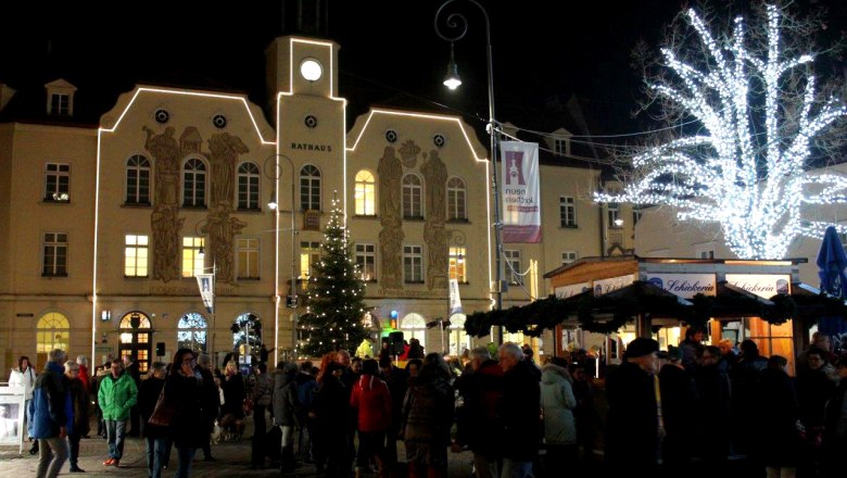 Main square, © Stadtgemeinde Neunkirchen Night shot of a busy Christmas market in front of an illuminated town hall with Christmas tree and tree of lights.