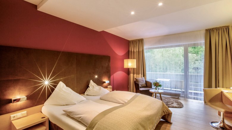 Room, © Hotel Krainerhütte Modern hotel room with double bed, red wall, large window and seating area.