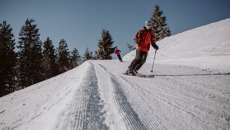 Unterberg ski area, © Schigebiet Unterberg | katischweiger.fotography Two skiers on a groomed slope in the Unterberg ski area.