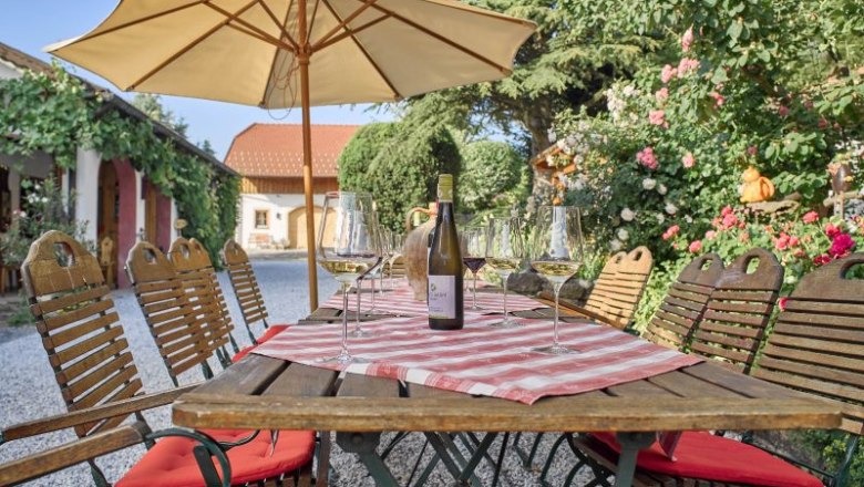 Inner courtyard Weinschwärmerei, © Florian Schulte A table in the courtyard with a bottle of wine and glasses, surrounded by plants and a parasol.