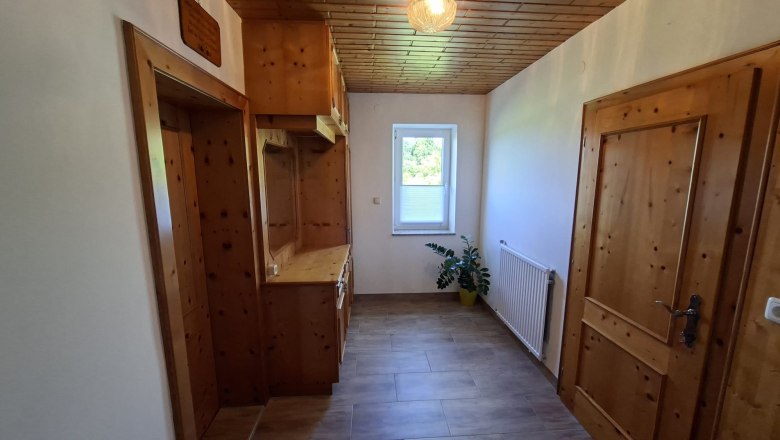 Anteroom, © Ferienwohnung Penz Stolzenthal, Fotograf Hermine Penz A narrow hallway with wooden furniture, a plant and a window with a view outside.