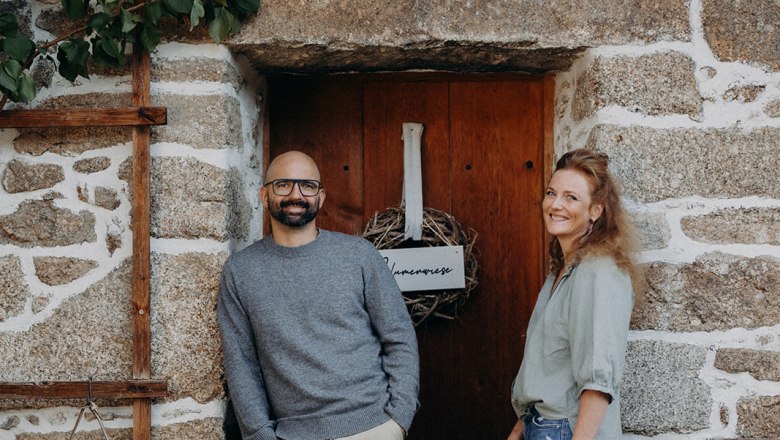 Aigen13, © Verena Schierl Two people are standing in front of a rustic stone house wall with a wooden door.