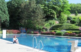 Waldbad Wölbling, © Marktgemeinde Wölbling Woman sitting at the edge of an outdoor swimming pool with forest in the background.