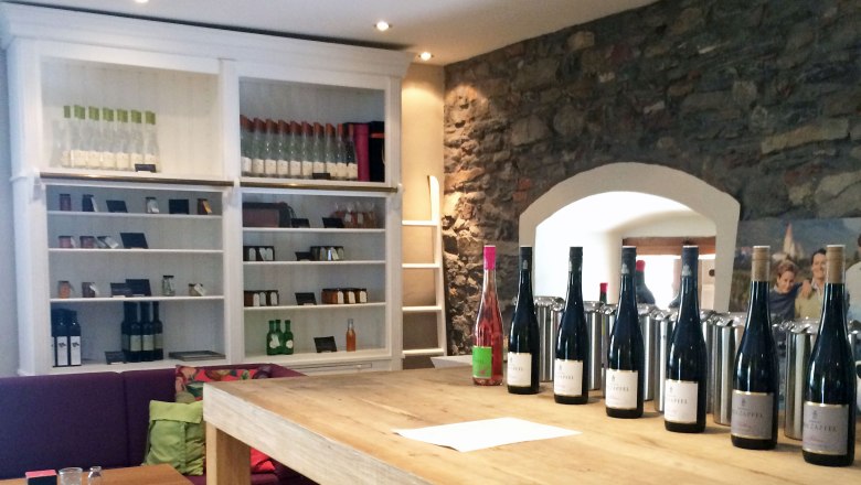 Tasting room, © Julia Schild Tasting room with wine bottles on a wooden table and shelves in the background.