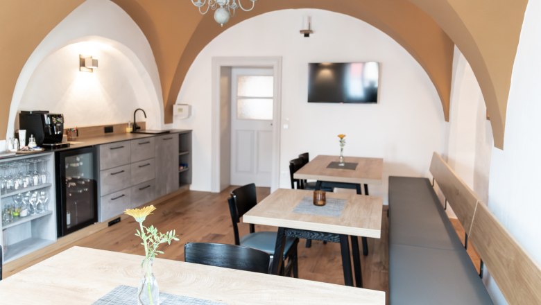 Breakfast room and lounge, © Fam. Teufelsbauer A cozy breakfast room with wooden tables, chairs and a bench. A TV hangs on the wall and there is a kitchenette with a coffee machine.