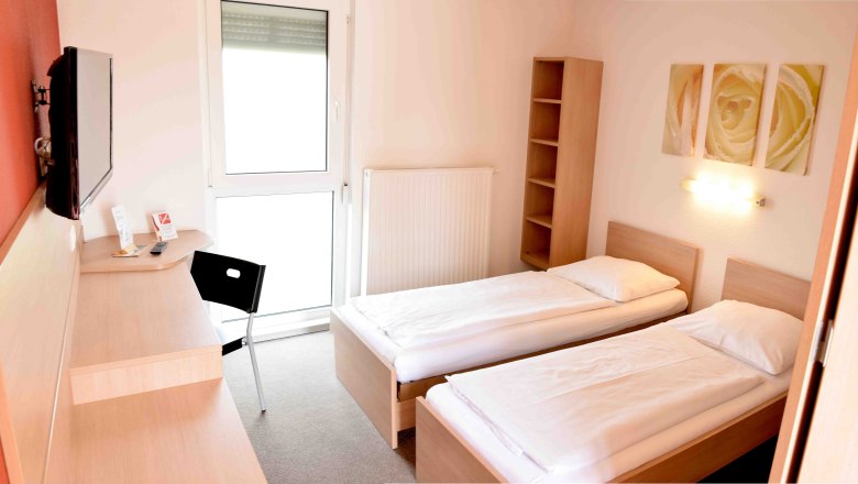 Motel room, © Motel Angern A simple motel room with two single beds, a desk, a chair and a TV on the wall.