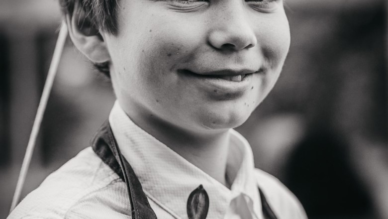 Junior Pölzer in service, © Monika Pölzer A boy in an apron labeled "Adam-Mühle" smiles at the camera.