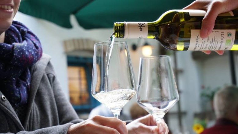 Tasting, © Bio-Weinbau Killmeyer Wine is poured into a glass while one person holds it.