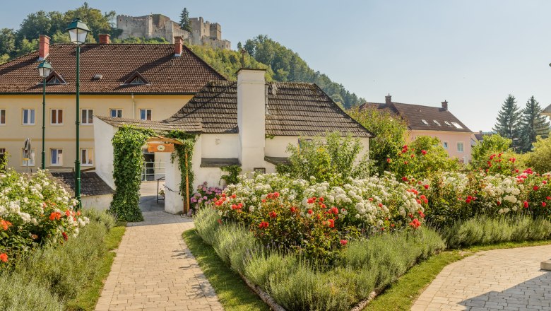 Kirchschlag rose garden, © Im Auftrag von Newman& Co fotografie& bildkonzept KG A well-tended rose garden with red and white roses and a castle on a hill in the background.