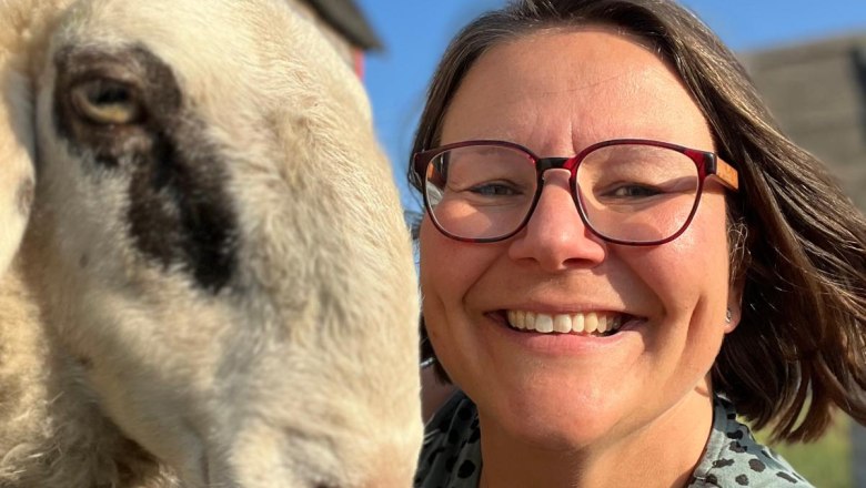 Cuddling experience with sheep, © Sabine Valis Woman with glasses smiles next to a sheep in the sun.