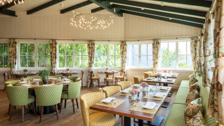 Conservatory, © Knappenhof Christian Husar A bright conservatory with covered tables, green chairs and large windows.